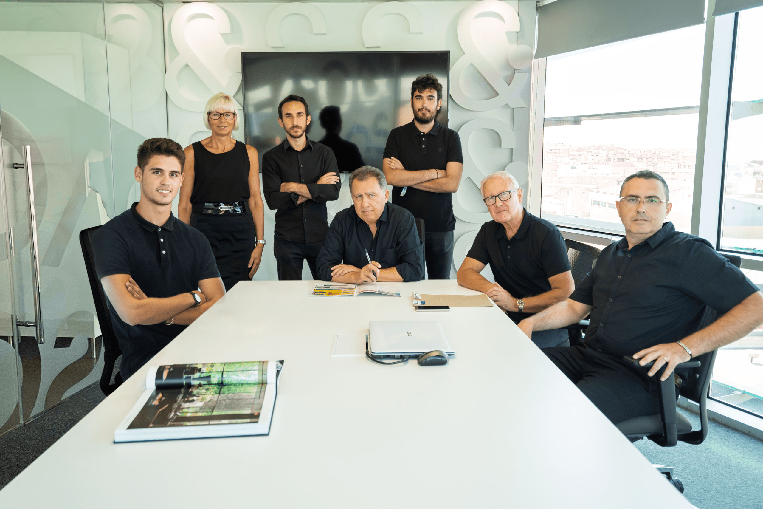 El equipo de Pacheco Arquitectos reunido en una sala de juntas, posando alrededor de una mesa de reuniones con documentos y portátiles.