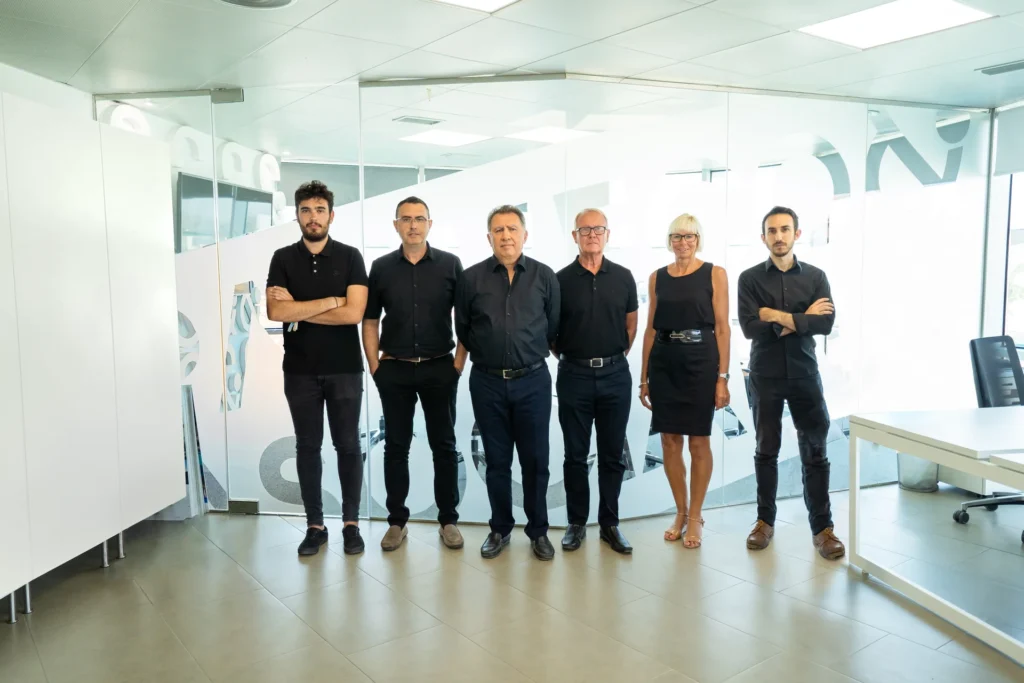 El equipo de Pacheco Arquitectos posando en línea dentro de sus oficinas, junto a una pared de cristal con diseño corporativo.