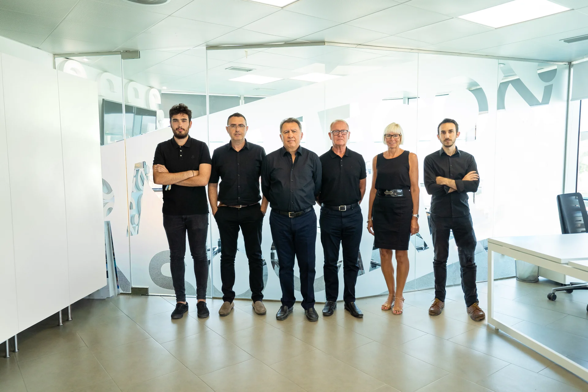 El equipo de Pacheco Arquitectos posando en línea dentro de sus oficinas, junto a una pared de cristal con diseño corporativo.