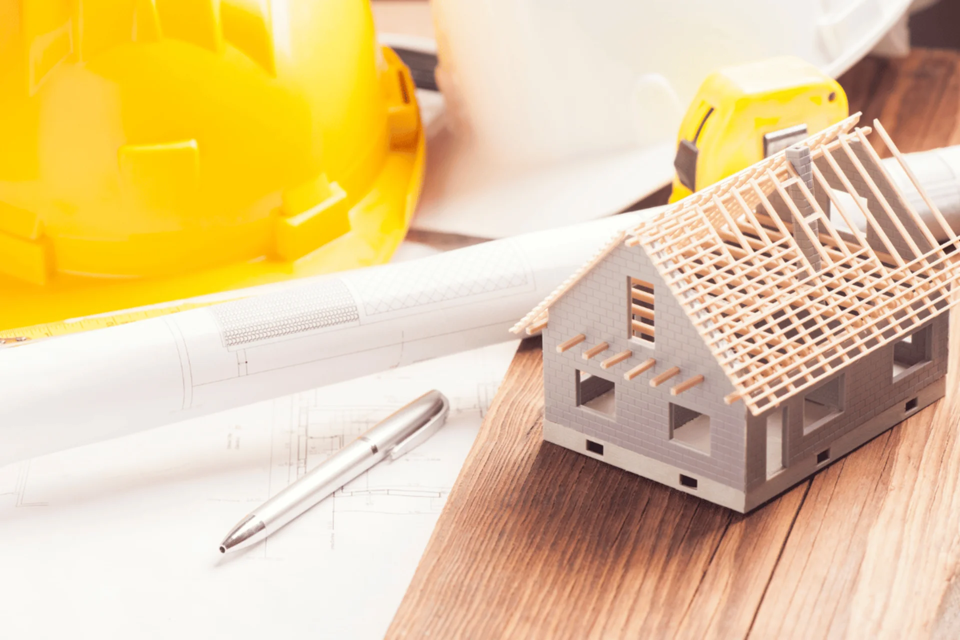 Maqueta de vivienda junto a casco de obra y planos, etapa inicial del proceso constructivo