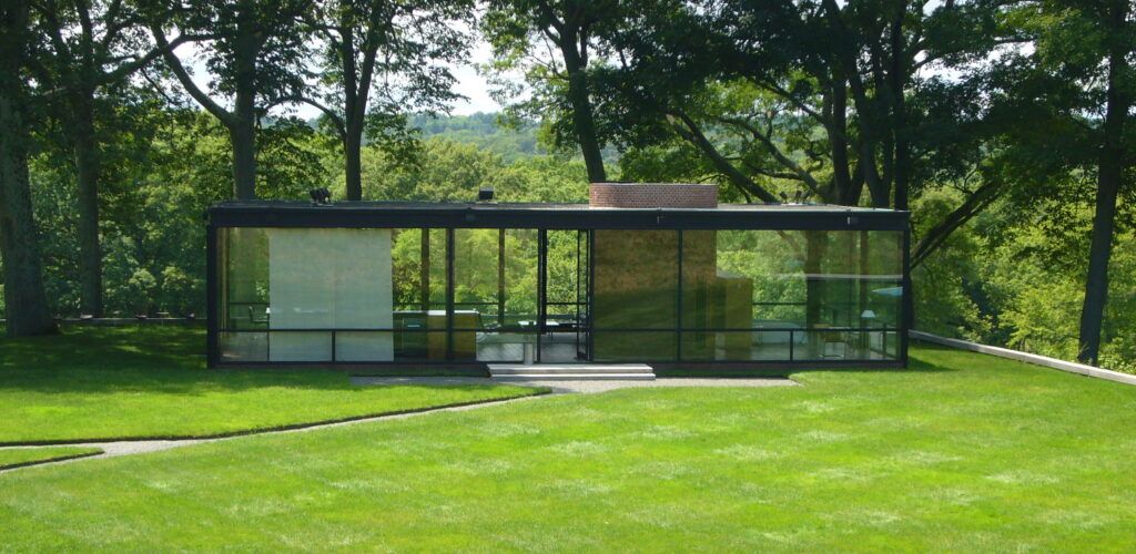 Vista frontal de la Glass House de Philip Johnson, ejemplo icónico de transparencia arquitectónica en medio de un entorno natural arbolado.
