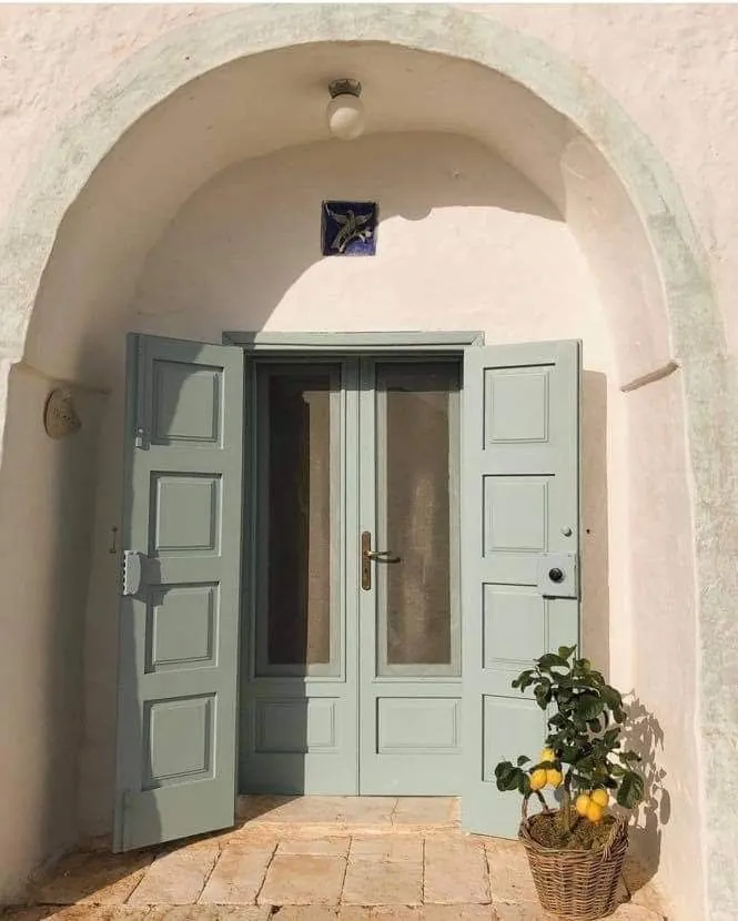 Diferencias entre la arquitectura vernácula de viviendas en Alicante y Murcia 4 Puerta doble de madera verde claro en fachada encalada con arco de medio punto y maceta con limonero, ejemplo de arquitectura vernácula mediterránea.