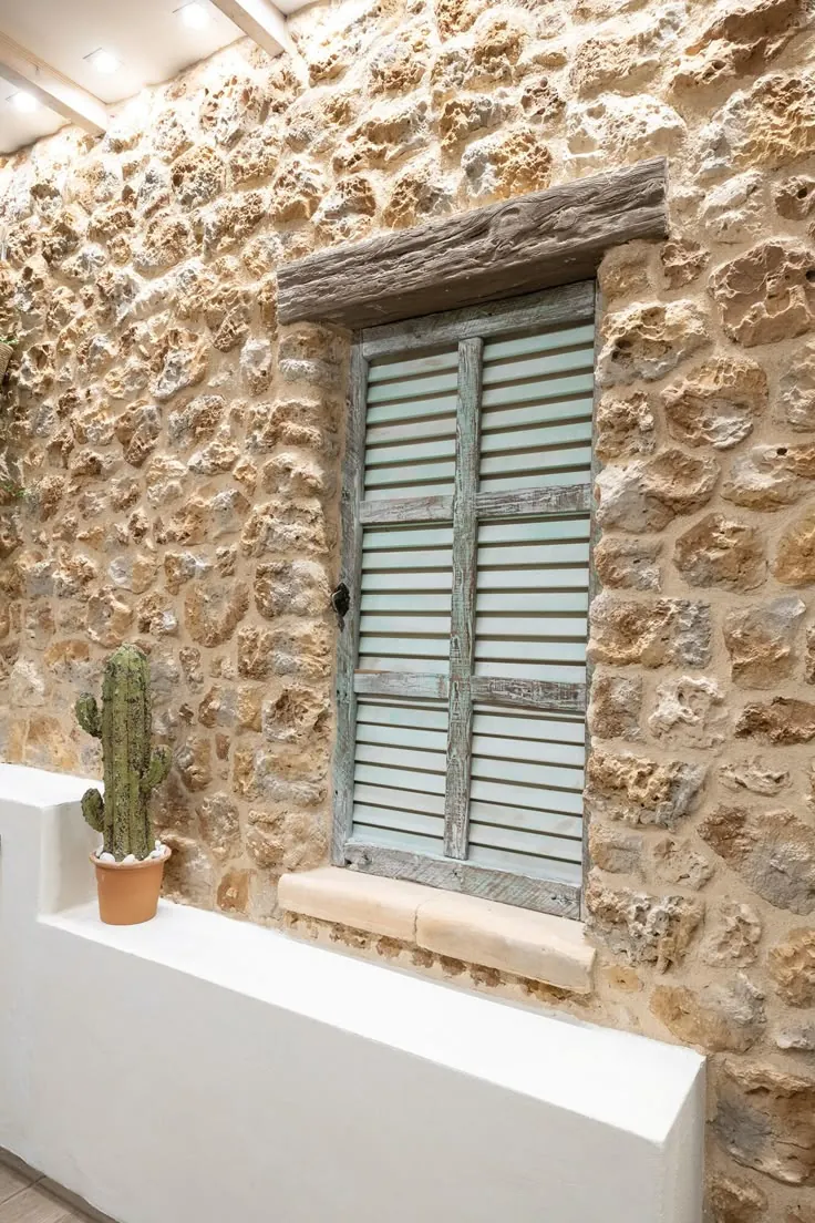 Diferencias entre la arquitectura vernácula de viviendas en Alicante y Murcia 3 Ventana con contraventanas de madera envejecida en fachada de piedra, ejemplo de arquitectura vernácula en el Mediterráneo.