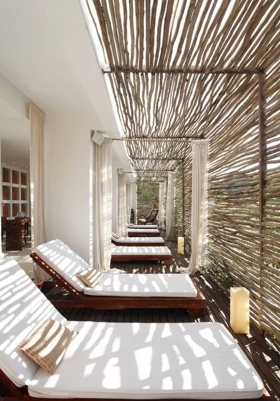 Tumbonas bajo pérgola de varas que proyecta sombras lineales con cortinas ligeras; vivienda compartida en Alicante y Murcia.